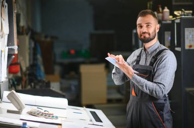 Çalışma üniformasında modern ofset baskı makinesi ve operatör ile ev içi yazdırma Kalite ve baskı süreci kontrol.