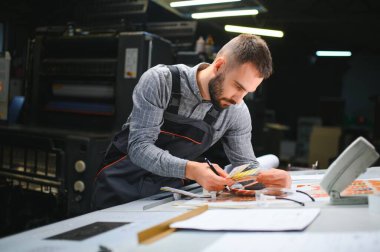 Yazıcı çalışanı yazdırma sürecinin kalitesini kontrol ediyor ve büyüteçle renkleri kontrol ediyor.