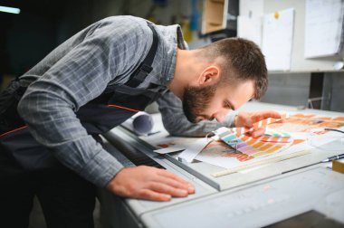 Yazıcı çalışanı yazdırma sürecinin kalitesini kontrol ediyor ve büyüteçle renkleri kontrol ediyor.