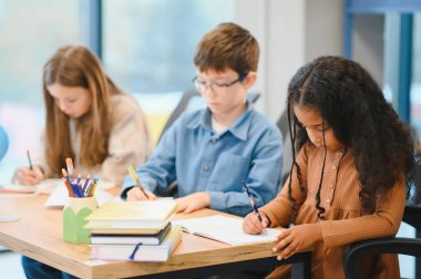 African American School Girl Writing Learning Sitting At Desk In Classroom Indoors. Diverse Children Having Class Taking Notes Indoor. Education And Knowledge. Selective Focus