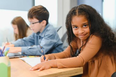 African American School Girl Writing Learning Sitting At Desk In Classroom Indoors. Diverse Children Having Class Taking Notes Indoor. Education And Knowledge. Selective Focus