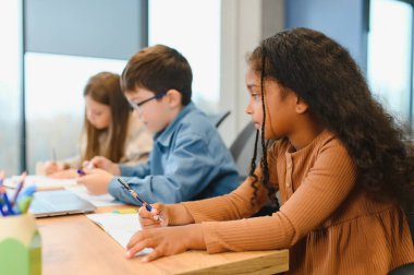 African American School Girl Writing Learning Sitting At Desk In Classroom Indoors. Diverse Children Having Class Taking Notes Indoor. Education And Knowledge. Selective Focus