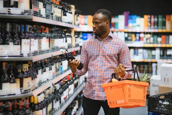 African American man in grocery store buying wine.