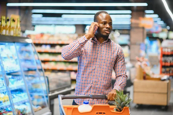 African American Man Talking On Cellphone Chatting While Shopping Groceries In Supermarket.