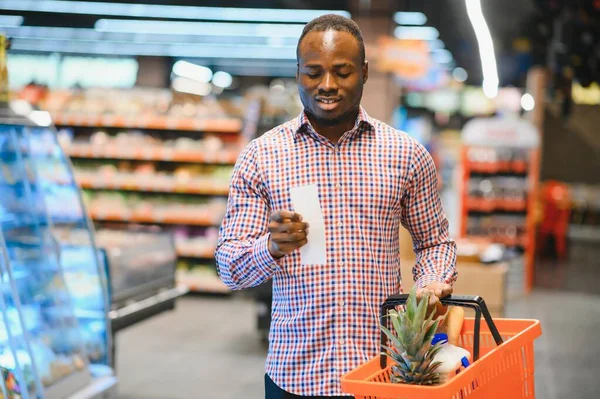 stock image Surprised African-American man looks at receipt total in sales check holding paper bag.