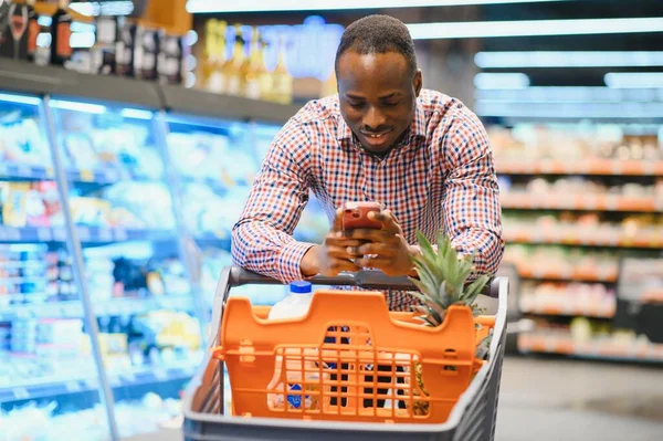 African American Man Talking On Cellphone Chatting While Shopping Groceries In Supermarket.
