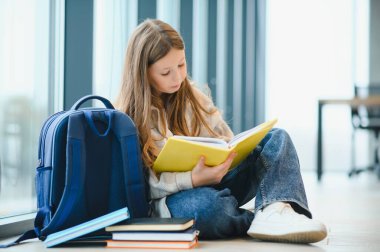 Güzel liseli kız pencerenin yanında oturmuş kitap okurken gülümsüyor..