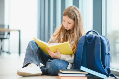 Güzel liseli kız pencerenin yanında oturmuş kitap okurken gülümsüyor..