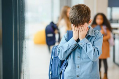 Okuldaki üzgün çocuk elleriyle yüzünü örtüyor. Okulda zorbalık..
