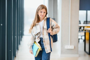 Okulun koridorunda duran, elinde notlar tutan küçük güzel bir kız öğrenci. Komik ve mutlu kız kameraya gülümsüyor, ilkokul derslerinden sonra dinleniyor..