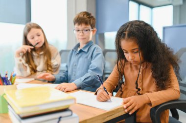 African American School Girl Writing Learning Sitting At Desk In Classroom Indoors. Diverse Children Having Class Taking Notes Indoor. Education And Knowledge. Selective Focus