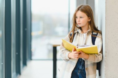 Liseli kız ayakta okulda koridor içinde defter ile gülümseyen portresi.