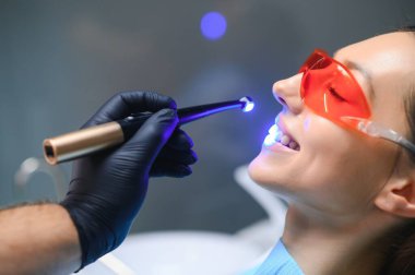 Young woman getting dental filling drying procedure with curing UV light at dental clinic.