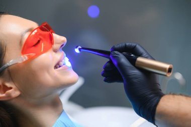 Young woman getting dental filling drying procedure with curing UV light at dental clinic.