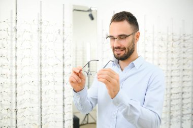 Genç adam optik dükkanında gözlük seçiyor..