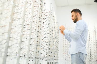 Genç adam optik dükkanında gözlük seçiyor..