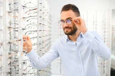 Sağlık, görme ve görme duyusu kavramı. Optik mağazasında gözlük seçen mutlu adam, seçici odaklı..