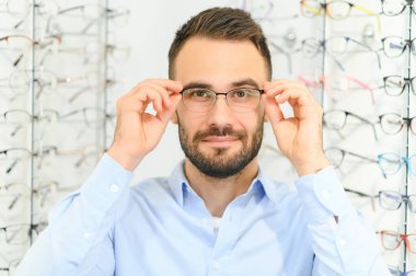 Sağlık, görme ve görme duyusu kavramı. Optik mağazasında gözlük seçen mutlu adam, seçici odaklı..