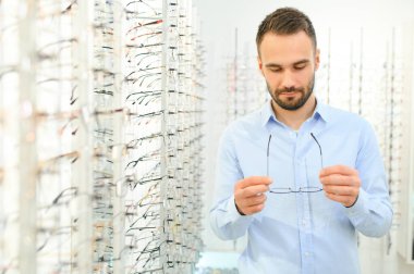 Sağlık, görme ve görme duyusu kavramı. Optik mağazasında gözlük seçen mutlu adam, seçici odaklı..