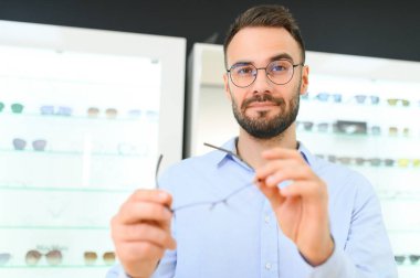 Genç adam optik dükkanında gözlük seçiyor..