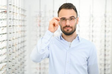 Genç adam optik dükkanında gözlük seçiyor..