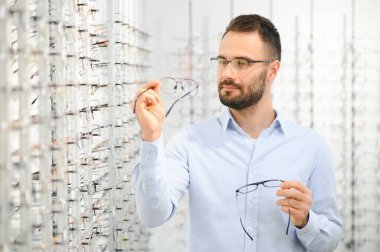 Genç adam optik dükkanında gözlük seçiyor..