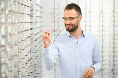Genç adam optik dükkanında gözlük seçiyor..