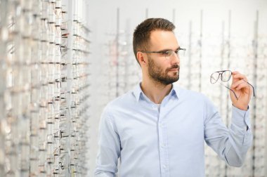 Genç adam optik dükkanında gözlük seçiyor..