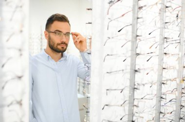 Genç adam optik dükkanında gözlük seçiyor..