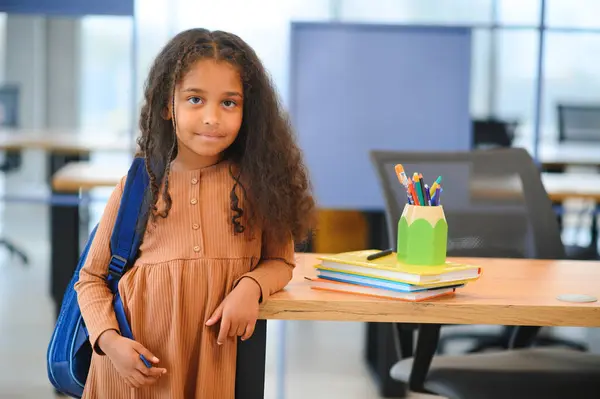 African-American girl in school looking at camera while standing in classroom, copy space.