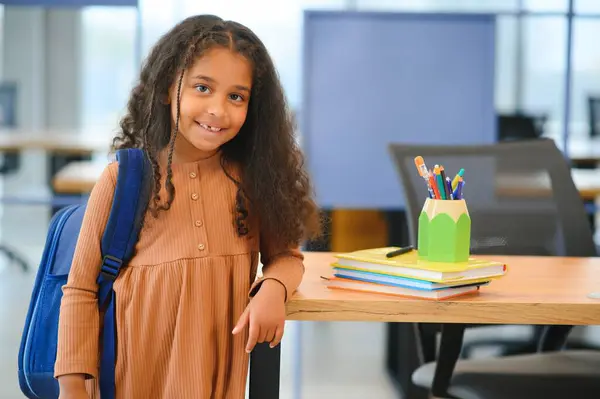 African-American girl in school looking at camera while standing in classroom, copy space.