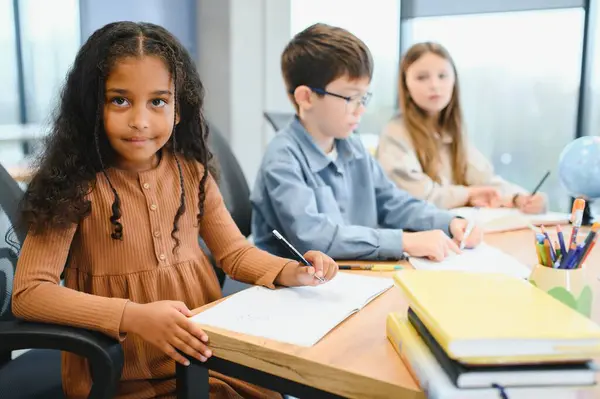 African American School Girl Writing Learning Sitting At Desk In Classroom Indoors. Diverse Children Having Class Taking Notes Indoor. Education And Knowledge. Selective Focus