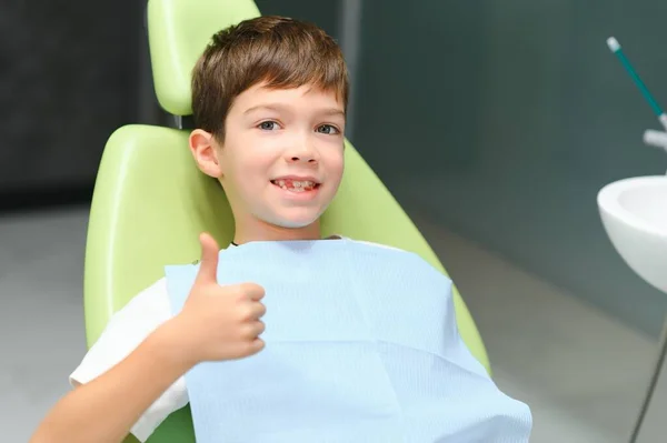 Little boy sits on dentist\'s chair in good mood after dental procedures. Young patient with healthy teeth.