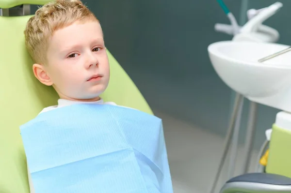 Scared red-haired boy crying at reception at dentist in dental chair. Pediatric dentistry.