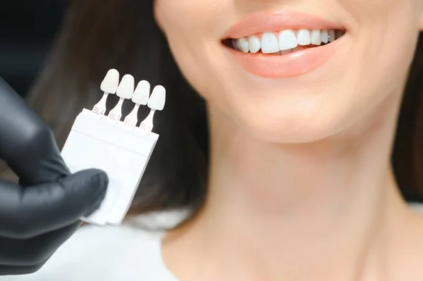 Dentist checking and selecting color of young woman\'s teeth.