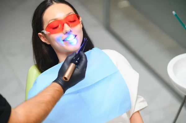 Young woman getting dental filling drying procedure with curing UV light at dental clinic.