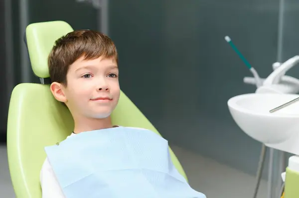 Little boy sits on dentist's chair in good mood after dental procedures. Young patient with healthy teeth.