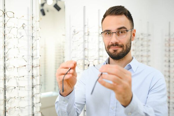 Young man choosing spectacles at optic shop.