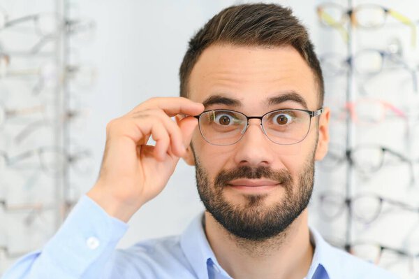Healthcare, Eyesight And Vision Concept. Happy man choosing glasses at optics store, selective focus.