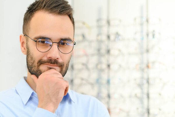 Young man choosing spectacles at optic shop.
