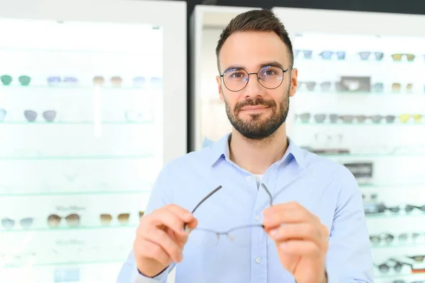 Healthcare, Eyesight And Vision Concept. Happy man choosing glasses at optics store, selective focus.