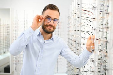Genç adam optik dükkanında gözlük seçiyor..