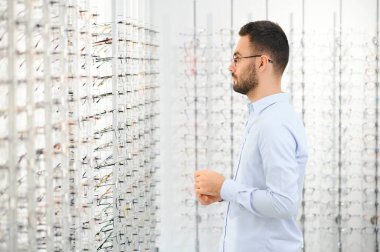 Genç adam optik dükkanında gözlük seçiyor..