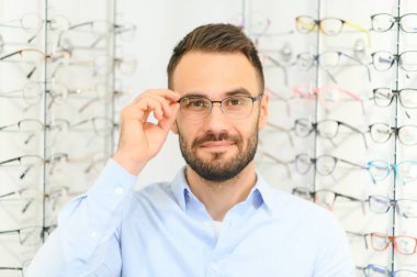 Genç adam optik dükkanında gözlük seçiyor..