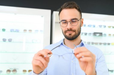 Genç adam optik dükkanında gözlük seçiyor..