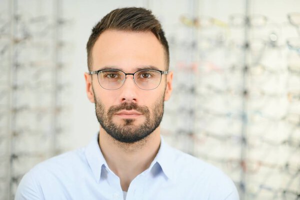 Young man choosing spectacles at optic shop.