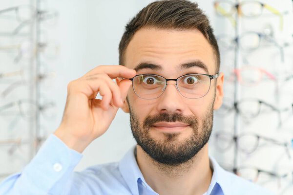 Young man choosing spectacles at optic shop.