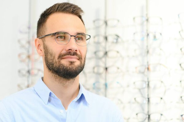 Young man choosing spectacles at optic shop.