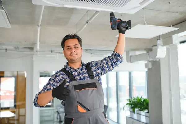 Concentrated young Indian engineer setting up air conditioner