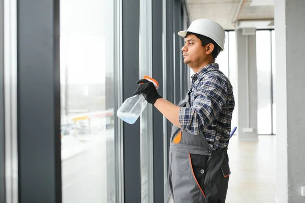 Male professional cleaning service worker in overalls cleans the windows and shop windows.